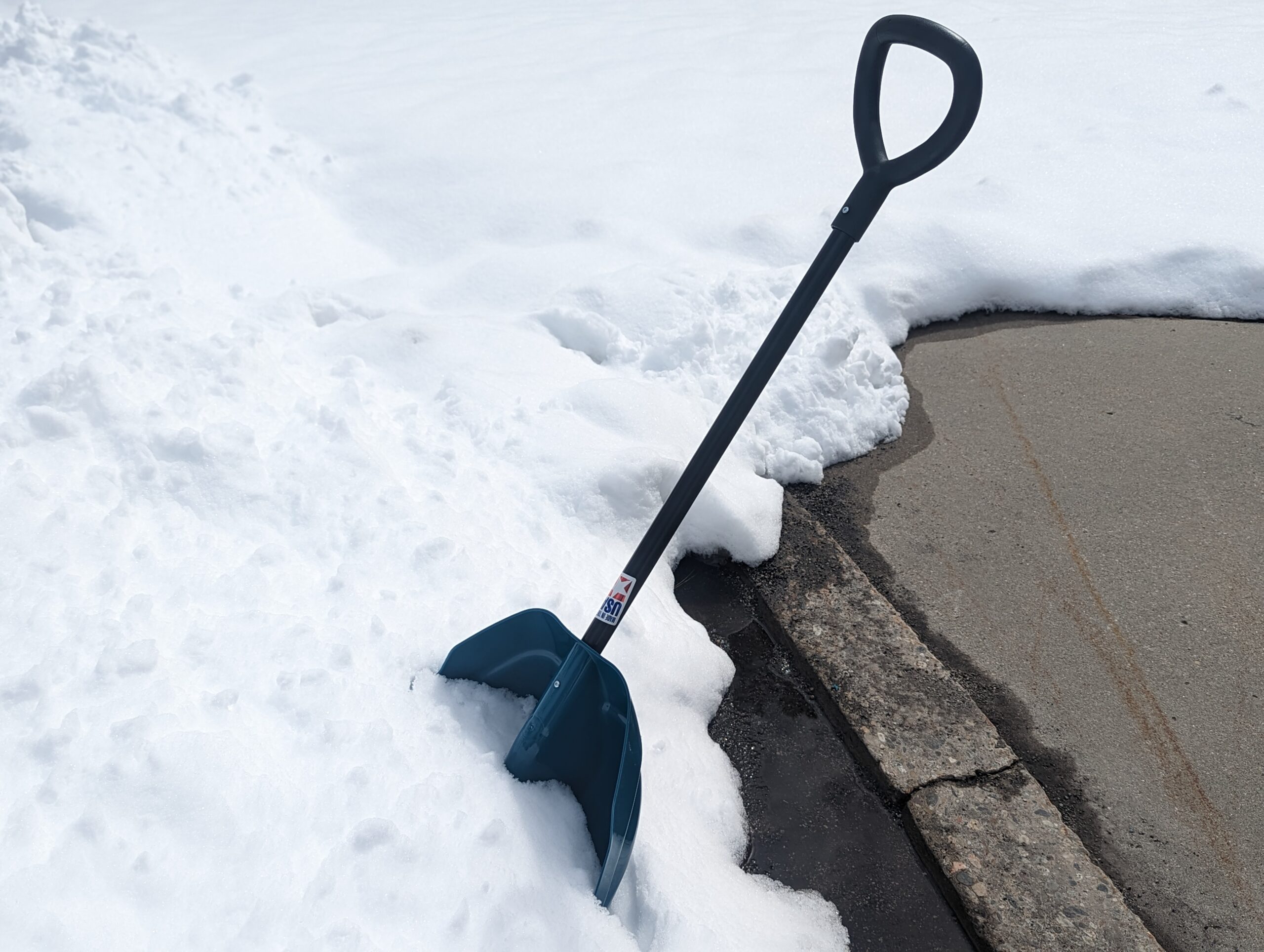 A snow shovel in the snow near a driveway