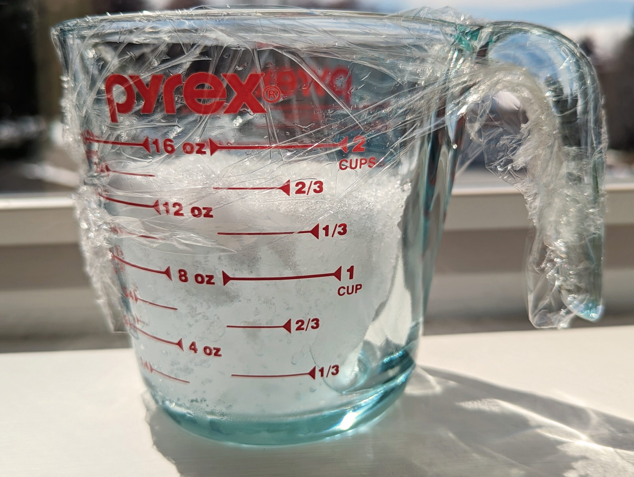 Pyrex cup with melting snow in it on a windowsill