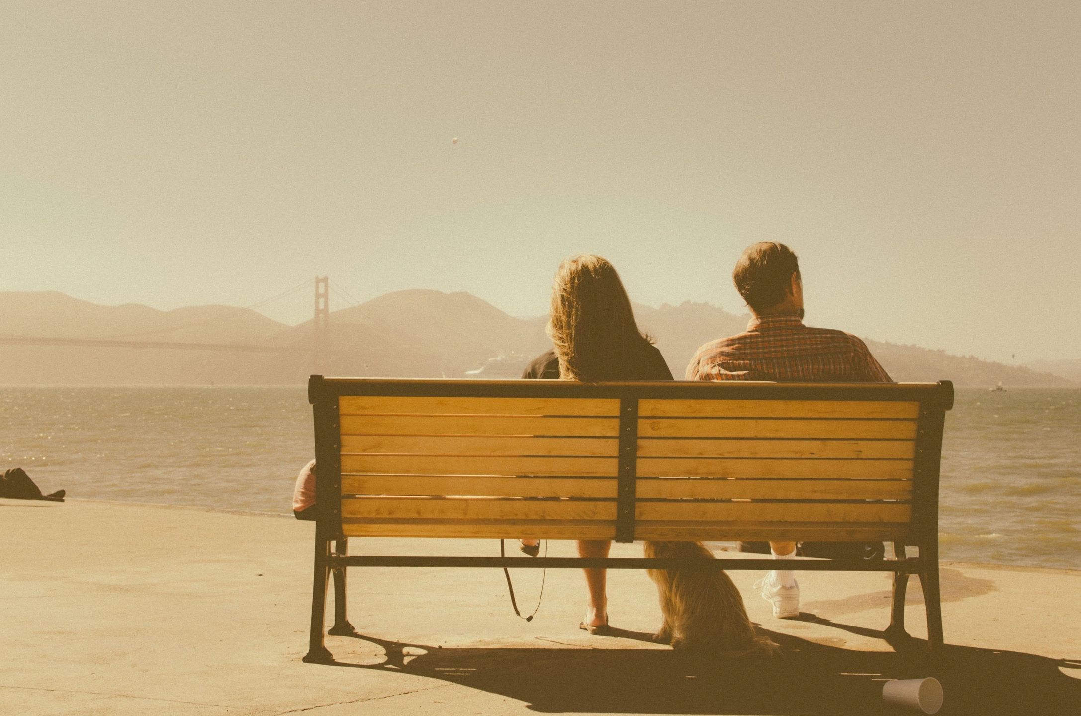 two people sitting on a park bench outside looking at the Golden Gate